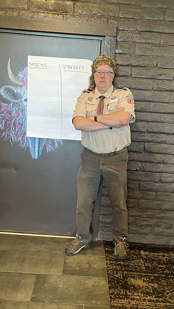 DLG Director Eric Bergman poses in his camp counselor costume with blank sheet titled Shocks and Stresses prior to conducting exercise that asks communities to consider the shocks and stresses they are facing