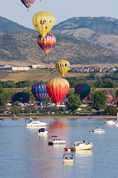 Several hot air balloons floating over lake full of boats in Colorado